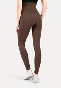 Brun leggings med høj talje lavet af et strækbart, glat materiale, med et tætsiddende design og ankel-længde sømme, kombineret med hvide sneakers.