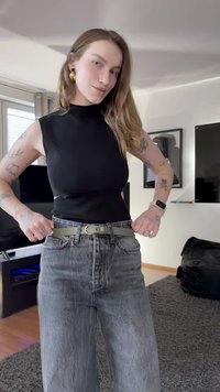 Top preto sem mangas combinado com jeans cinza escuro de cintura alta. Um cinto verde com fivela prateada acentua a cintura.