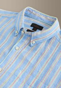 Chemise bleue boutonnée avec des rayures verticales multicolores, des boutons blancs et un col boutonné allongé à plat.