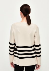 Beige tröja med en svart horisontell randdesign. Har rak passform, långa �ärmar och sidofickor. Slät textur.