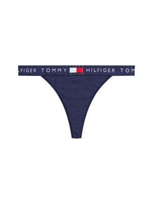 Navy blauwe stringonderbroek met een merk-elastasband waarop "TOMMY HILFIGER" in het wit staat, vergezeld van een gekleurd logo-accent. Zachte stoftextuur.