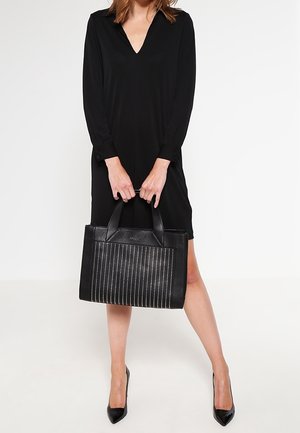 Černá kožená taška typu tote s cvočky v podobě svislých linií, pevnými držadly a strukturovaným tvarem. Taška má hladkou texturu a kovové doplňky.