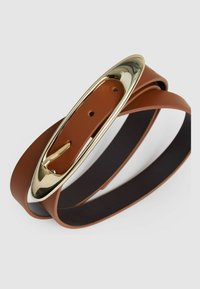 Brūns ādas josta ar zelta pārklājumu metāla sprādzi, kas ir ovāla formas ar izgriezumiem, izstrādāta ar divām slāņiem un redzamām caurumiem.