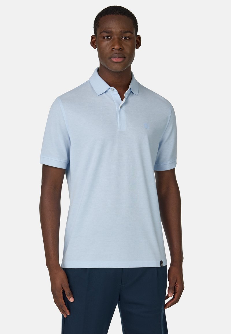 Polo de color azul claro hecho de una tela suave, con un cuello clásico, dos botones y un sutil logotipo en el lado izquierdo del pecho.