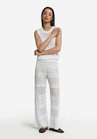 Biały top z dzianiny na szydełku z okrągłym dekoltem i szerokim, bezrękawnym krojem. Do tego szerokie spodnie z dzianiny na szydełku o wzorzystej fakturze.