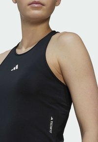 Fekete sportos trikó, illeszkedő szabással, sima anyagból készült. Fehér logó részletekkel és hátrafelé vágott kivágással a mozgás szabadságáért.
