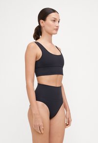 Black bikini top with a scoop neckline and wide straps, paired with high-waisted bikini bottoms. Smooth texture, minimalistic design.