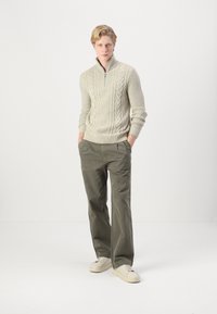 Maglione zip-up a maglia cable beige chiaro con maniche lunghe, abbinato a un paio di pantaloni verdi oliva rilassati e sneaker off-white.