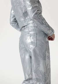 Giacca e pantaloni ricamati in argento con un motivo botanico, caratterizzati da un tessuto texturizzato e una lucentezza sottile, progettati con una linea aderente.