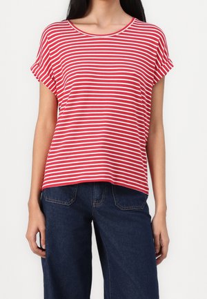 Femme portant un t-shirt à manches courtes rayé horizontalement rouge et blanc et un jean en denim bleu foncé, debout devant un fond blanc.