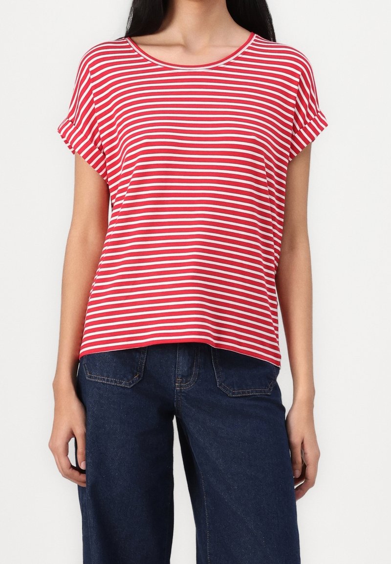 Femme portant un t-shirt à manches courtes rayé horizontalement rouge et blanc et un jean en denim bleu foncé, debout devant un fond blanc.