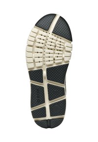 Semelle de sneaker en caoutchouc noir et crème avec des motifs de grip texturés, des trous de ventilation et un branding visible. Conçue pour la traction et le confort.