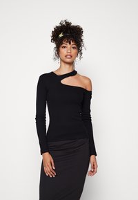 Zwarte top met lange mouwen en een off-shoulder uitsnijding, gemaakt van elastische stof. Model draagt een zwarte rok die een slanke silhoeët benadrukt.