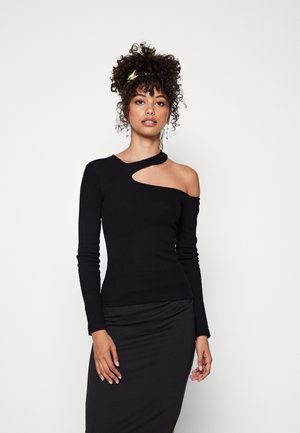 Black long-sleeve top with an off-shoulder cutout, made of fitted fabric. Model wears a black skirt, showcasing a sleek silhouette.