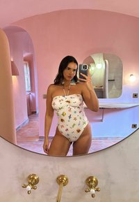 Strapless eendelig badpak in crème met een kleurrijke marine-thema print. Kenmerken zijn een gedraaide voorkant en een hoge snit bij de benen.