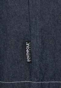 Tissu en denim bleu foncé avec motif de tissage diagonal, comprenant une étiquette noire et blanche "SOUTHPOLE ORIGINALS" cousue au bord.