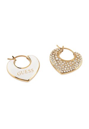 Gouden hartvormige oorbellen; de ene heeft witte emaille met het "GUESS" logo, de andere heeft een oppervlak van sprankelende strass.