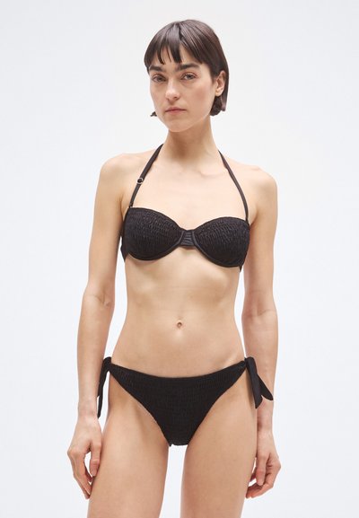 Black bikini made of textured fabric; bandeau top with underwire and adjustable halter straps, tied sides on the bottom, simple design.