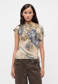 Korte mouwen top in een beige stof met blauwe en bruine abstracte patronen. Bevat een geraffineerde details aan de zijkant en een ronde halslijn.