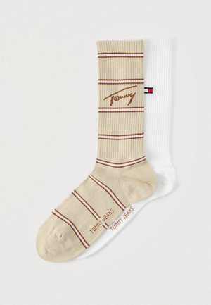 Triibulised sokid, millel on beež kangas punaste triipudega ja logo, koos ühevärvilise valge soonilise tekstuuri ja logoga sokiga.