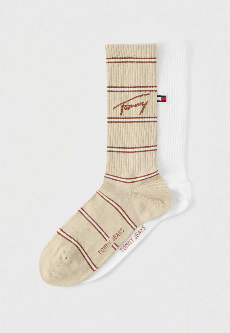 Ριγέ κάλτσες με μπεζ ύφασμα, κόκκινες ρίγες και λογότυπο, συνδυασμένες με μονόχρωμη λευκή κάλτσα με ραβδωτή υφή και λεπτομέρεια λογότυπου.
