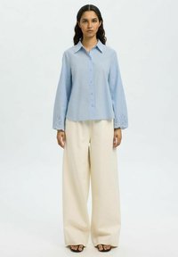 Hele sinine nööpidega särk pika varrukaga, millel on tikandid mansettidel. Kombineeritud laia säärtega kreemiste pükstega.