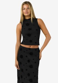 Svart crop top och matchande kjol med blommönster, tillverkad av mjukt tyg med en figurnära design och en blygsam halsringning.