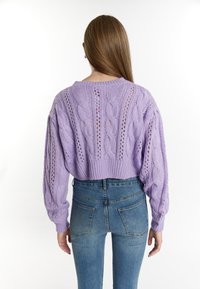 Gekürzter lila Kabelstrickpullover mit durchbrochenen Mustern und langen Ärmeln, kombiniert mit hochgeschnittenen blauen Jeans.