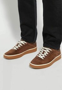 Brown suede sneakers with white laces, gum rubber sole, and a smooth accent near the heel, complemented by a low-profile design.