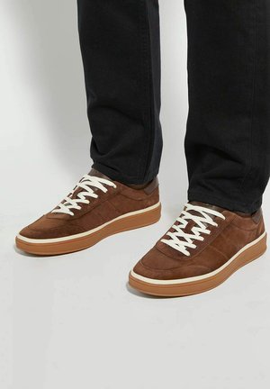 Brown suede sneakers with white laces, gum rubber sole, and a smooth accent near the heel, complemented by a low-profile design.