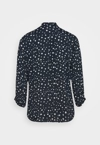 Chemise bleu marine à manches longues avec des pois blancs irréguliers, poignets boutonnés et ourlet arrondi, vue de dos.