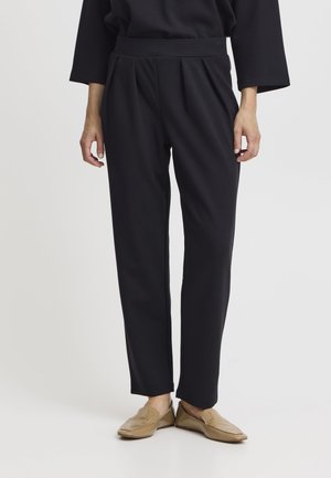 Pantaloni neri a sigaretta realizzati in tessuto morbido, con un'alta vita e pieghe frontali. Abbinati a scarpe slip-on marrone chiaro.
