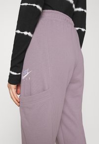 Pantaloni della tuta viola con una texture morbida, dotati di tasca laterale e logo "Nike Air" ricamato. Vita elastica per una vestibilità sicura.