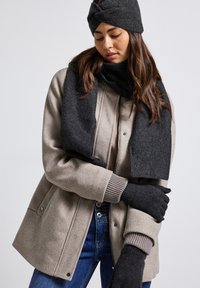 Abrigo de lana gris claro con un cuello acanalado, combinado con una bufanda oscura y guantes. La bufanda presenta una textura sutil y los guantes son de color negro sólido.