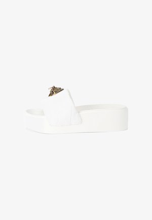 Sandale à plateforme blanche avec large bride rembourrée et emblème décoratif doré sur la bride, vue de côté sur fond blanc.