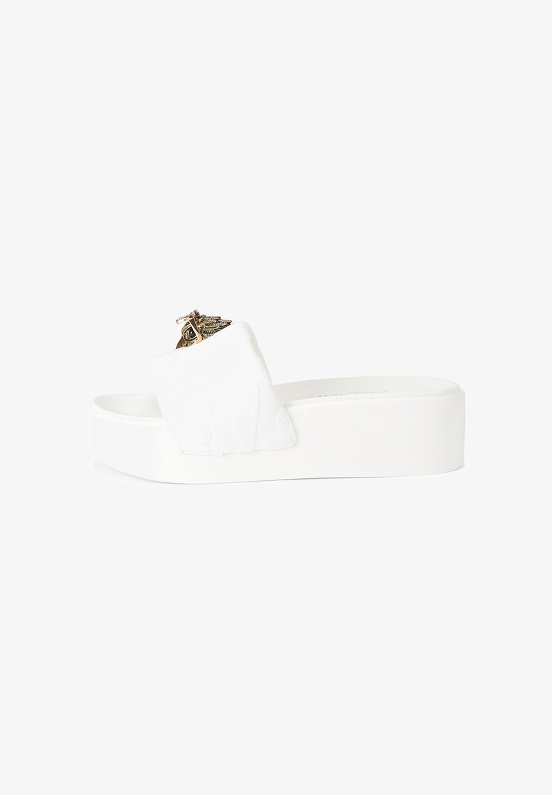 Sandale à plateforme blanche avec large bride rembourrée et emblème décoratif doré sur la bride, vue de côté sur fond blanc.