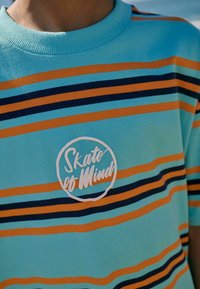 Krátký rukáv, tyrkysová bavlněná košile s oranžovými a námořnickými vodorovnými pruhy. Obsahuje kulaté bílé logo s nápisem "Skate of Mind."