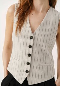 Vaaleanharmaa pellavainen liivi, jossa pystysuorat mustat raidat. Siinä on V-aukko, viisi nappia ja etutaskut. Räätälöity istuvuus, ilman hihoja.