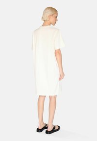 Cream-colored oversized t-shirt dress in soft fabric, featuring short sleeves and a round neckline, paired with black flat sandals.
