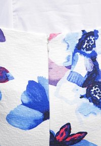 Floraler Reißverschluss aus Stoff mit großen blauen und lila Blüten auf weißem strukturiertem Hintergrund und einem glatten Reißverschluss in der Mitte.