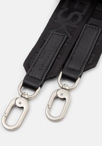 Musta kangashihna nahkaesineillä, metallilukoilla kummassakin päässä. Painatettu brändäys. Sileä pinta, tukeva rakenne.