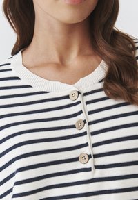 Striped top featuring navy and white horizontal lines, soft knit material, ribbed collar, and three wooden buttons at the neckline.