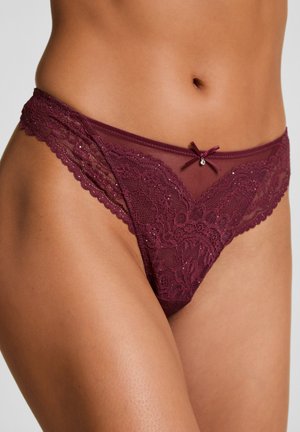 Vrouw in bourgondische kant bikini-stijl ondergoed met een klein strikje en juweel detail aan de voorkant van de tailleband.