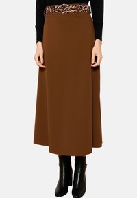 Bruine, vloeiende midilange rok van zacht materiaal, met een riem met luipaardprint. Gecombineerd met zwarte enkellaarzen met hak.