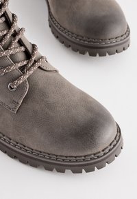 Botas de tobillo de ante gris con puntera redonda, parte superior texturizada y diseño de cordones. Con cordones en contraste en marrón y plata y suela de goma resistente.