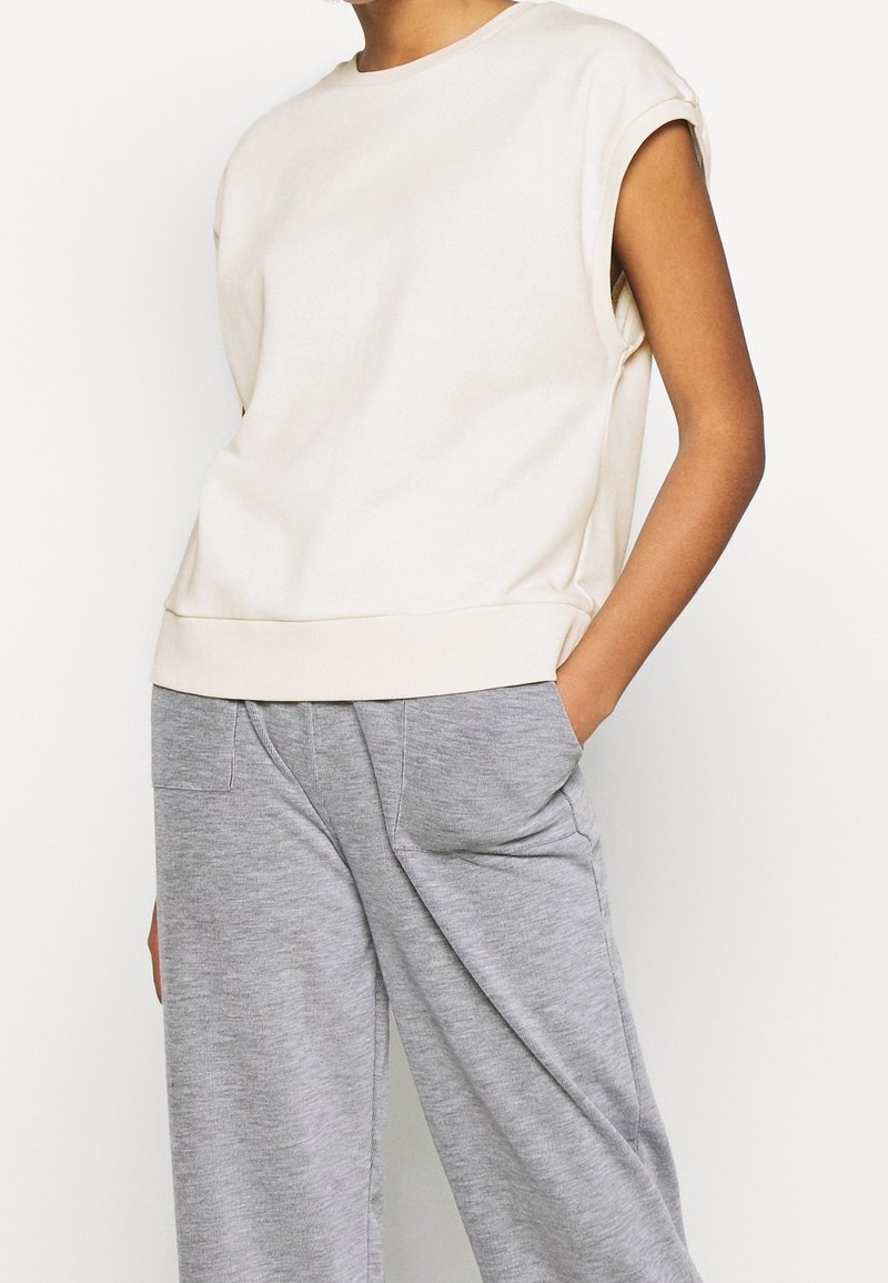 Sudadera beige de manga corta en tejido suave con cuello redondo y corte relajado. Combinada con pantalones de chándal grises, holgados y con bolsillos.