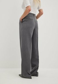 Wide-leg gray trousers with a textured fabric, high waist, front and back pockets, and a tailored design. Features a clean, modern silhouette.