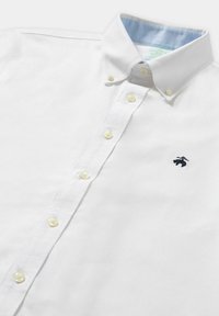 Bílá košile na knoflíky vyrobená z bavlny, s jemně modrým lemem na límci a žlutými knoflíky. Malé námořnické logo na hrudi.