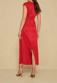 Robe midi rouge avec manches courtes, silhouette ajustée, tissu texturé et fente latérale. Associée à des talons dorés à brides et des accessoires minimalistes.