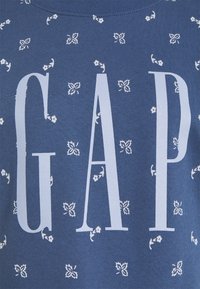 Donkerblauwe sweatshirt met witte bloemmotieven en een opvallend "GAP"-logo in dikke letters over de borst. Zachte stofstructuur.